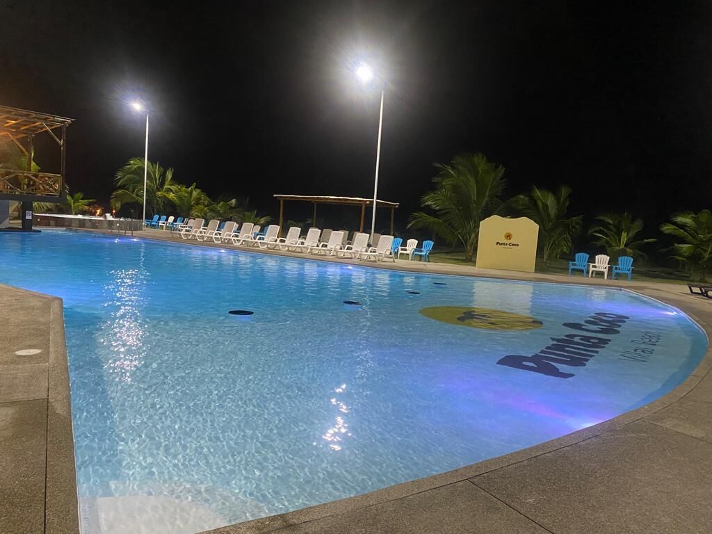 Ein Swimmingpool mit Liegestühlen und einer überdachten Liegefläche, umgeben von Palmen.