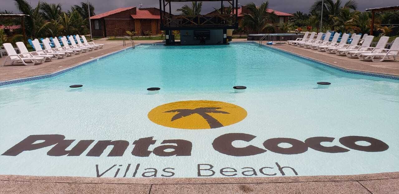 A swimming pool with lounge chairs and a logo for Punta Coco Villas Beach.