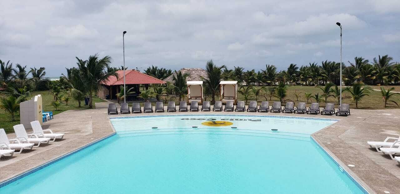 Una piscina con sillones de descanso y un edificio pequeño al fondo.