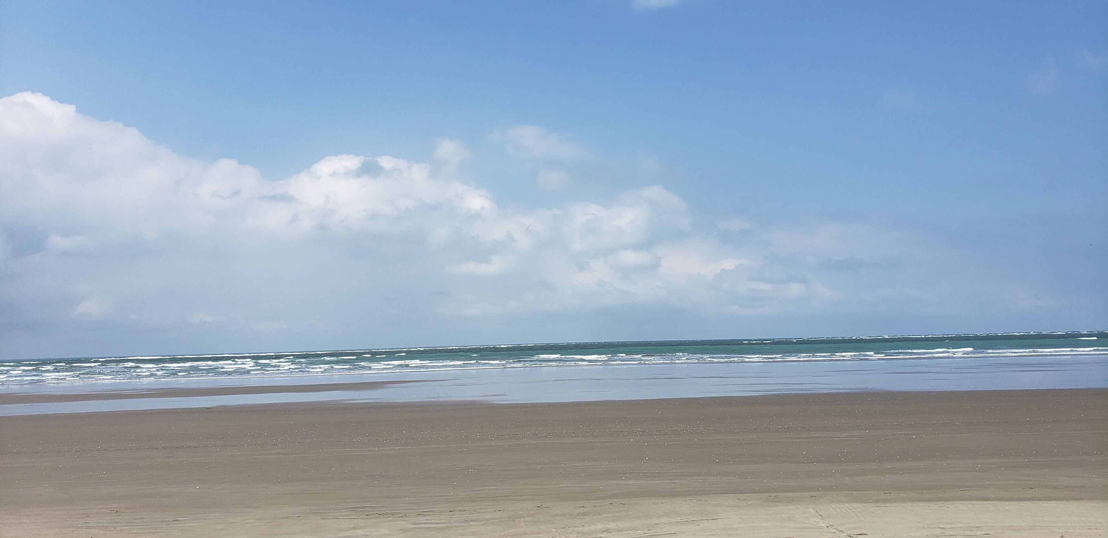 A beach with a wide sandy shore and a calm sea under a partly cloudy sky.