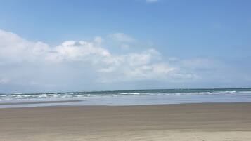 A beach with a wide sandy shore and a calm sea under a partly cloudy sky.