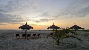 A beach with thatched umbrellas and lounge chairs facing the ocean at sunset. - PUNTA COCO VILLAS BEACH (Cojimies)