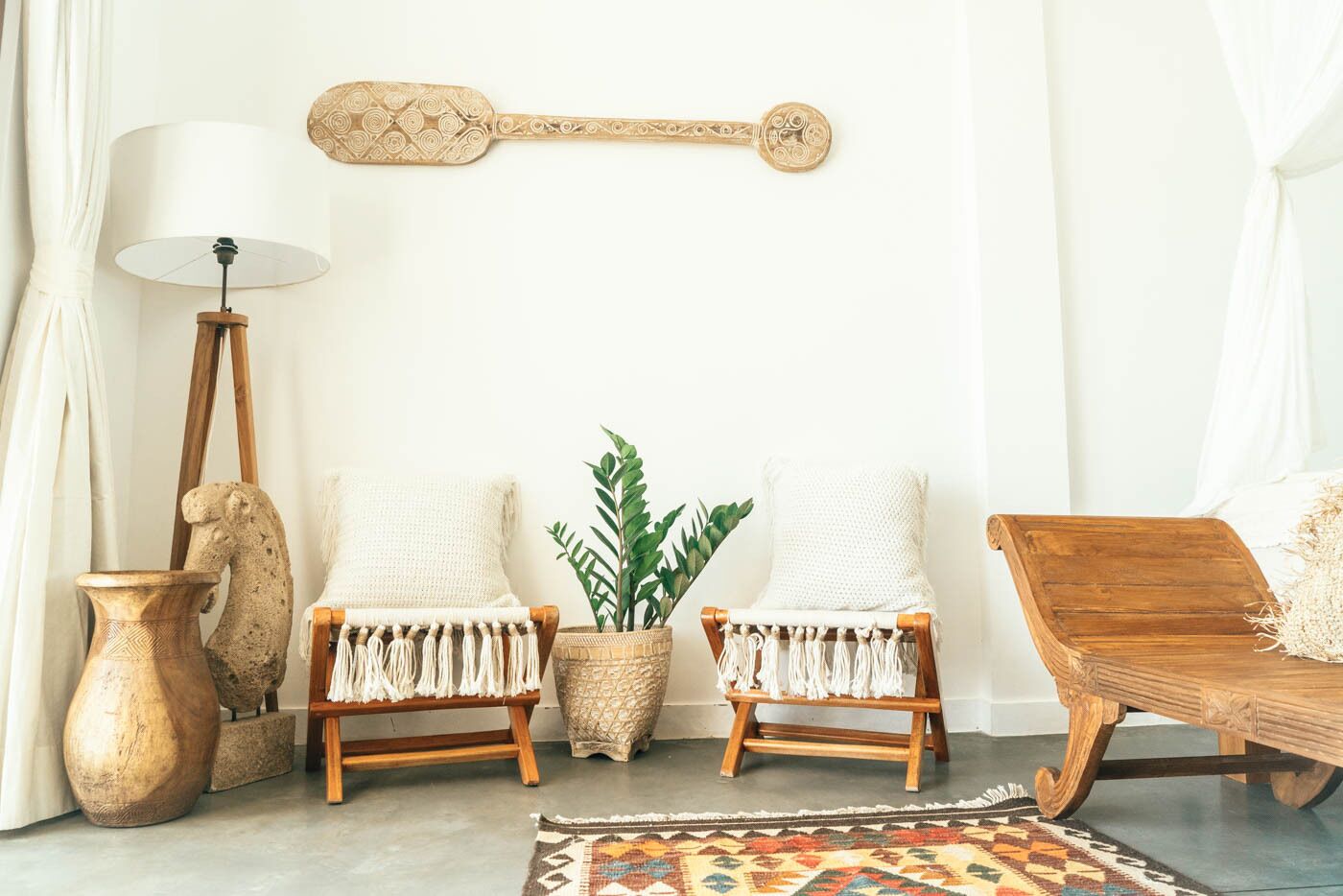 Una habitación con dos sillas blancas de fibras naturales, una mesita de madera, una lámpara de pie, un adorno en la pared y una alfombra estampada.