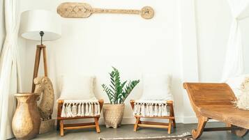 Una habitación con dos sillas blancas de fibras naturales, una mesita de madera, una lámpara de pie, un adorno en la pared y una alfombra estampada.
