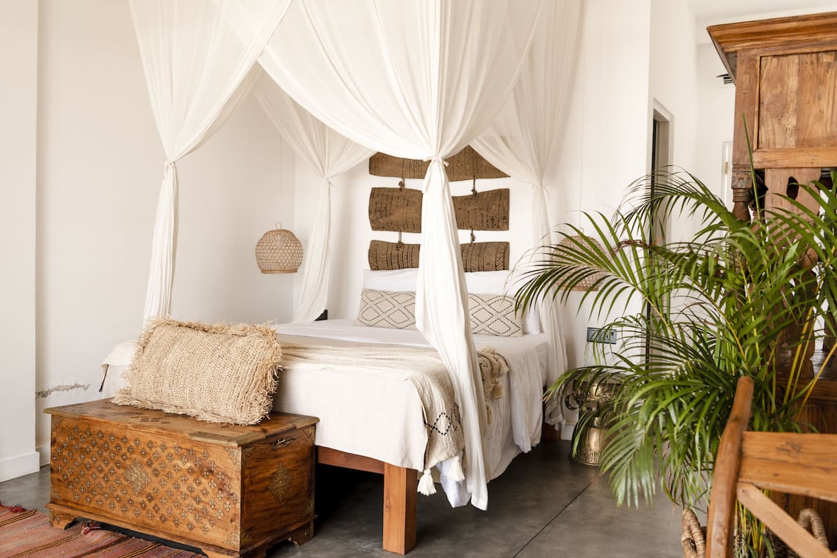 Een slaapkamer met een hemelbed, een houten kist en een grote kamerplant.