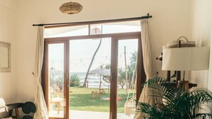 Une pièce dotée d’une grande porte-fenêtre coulissante qui donne sur une terrasse offrant une vue sur l’océan et sur une pelouse. On y trouve une lampe, une plante et un tableau encadré accroché au mur.
