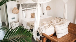 Une chambre avec un lit à baldaquin, un banc en bois et un panier tressé accroché au mur.