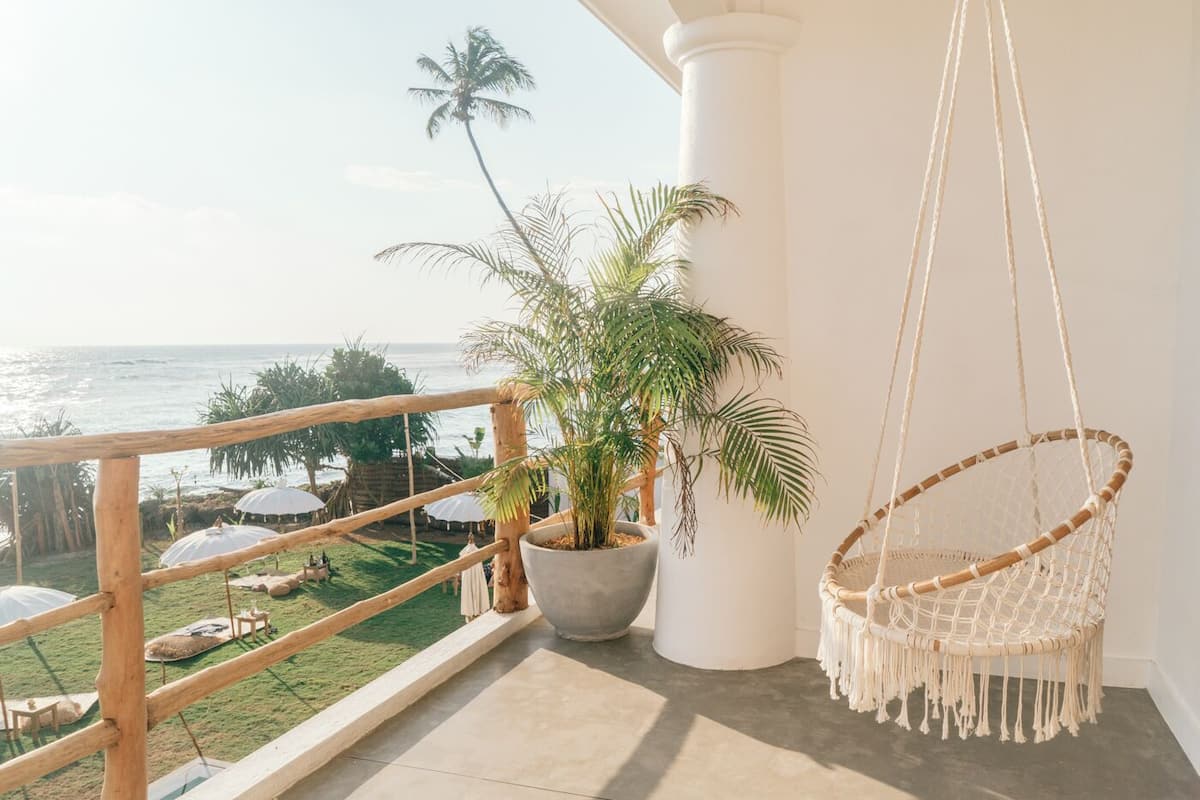 Een balkon met uitzicht op de oceaan, een hangstoel en een bloempot met plant.
