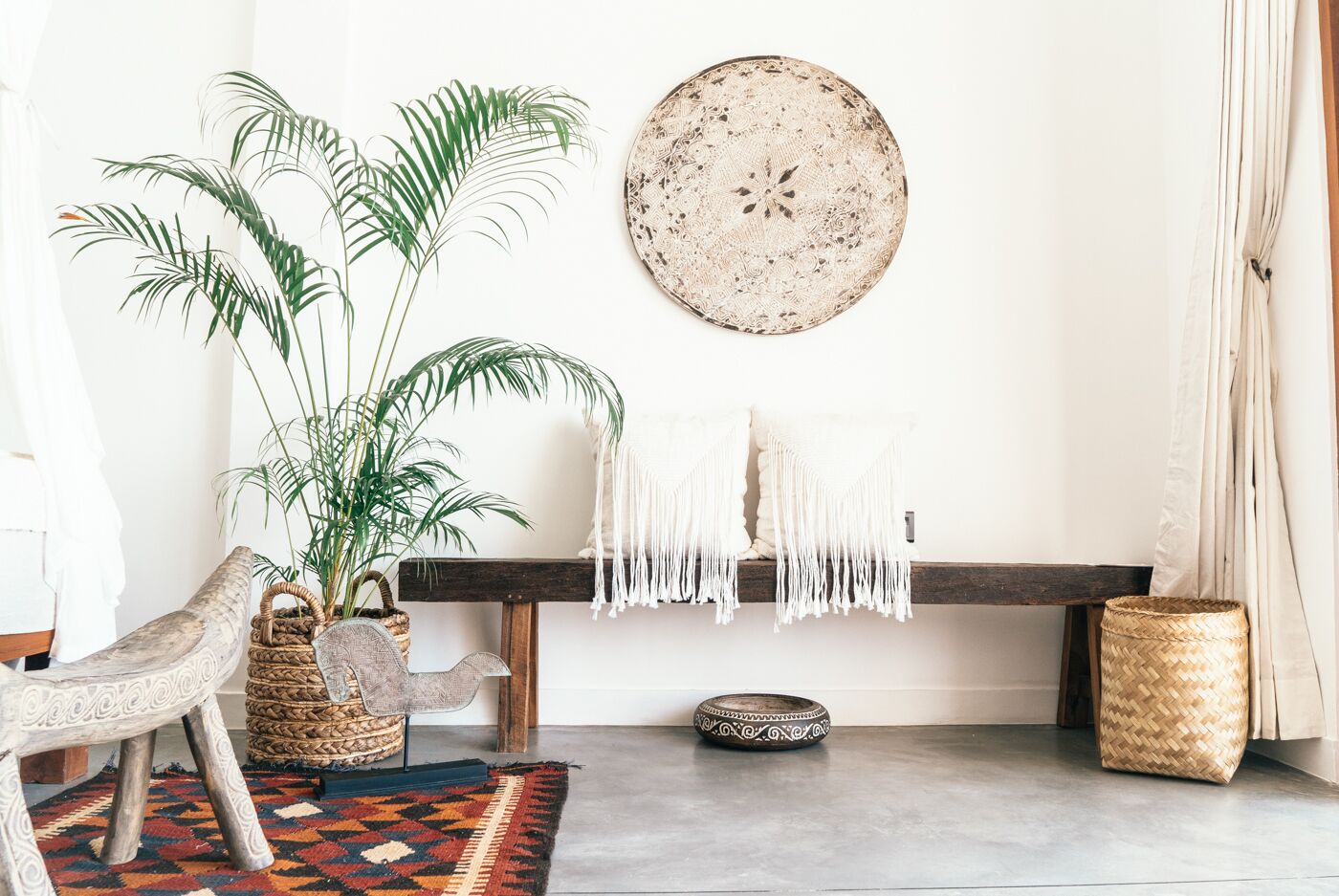 Un salon chaleureux avec un banc, une plante en pot, un panier tressé et une assiette décorative accrochée au mur.