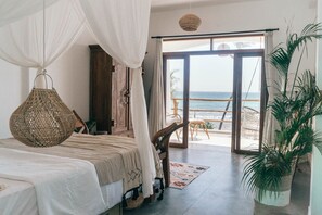 Une chambre avec un lit, une lampe suspendue, une vue sur la plage et une grande plante en pot.