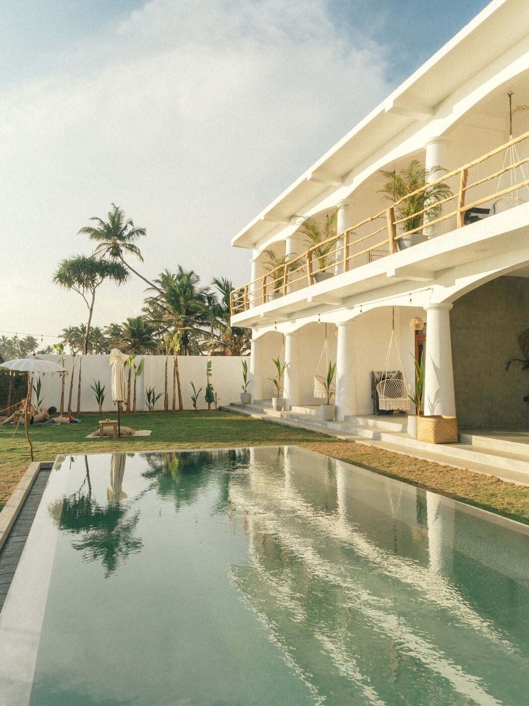 A modern resort with a swimming pool, outdoor seating, and palm trees.