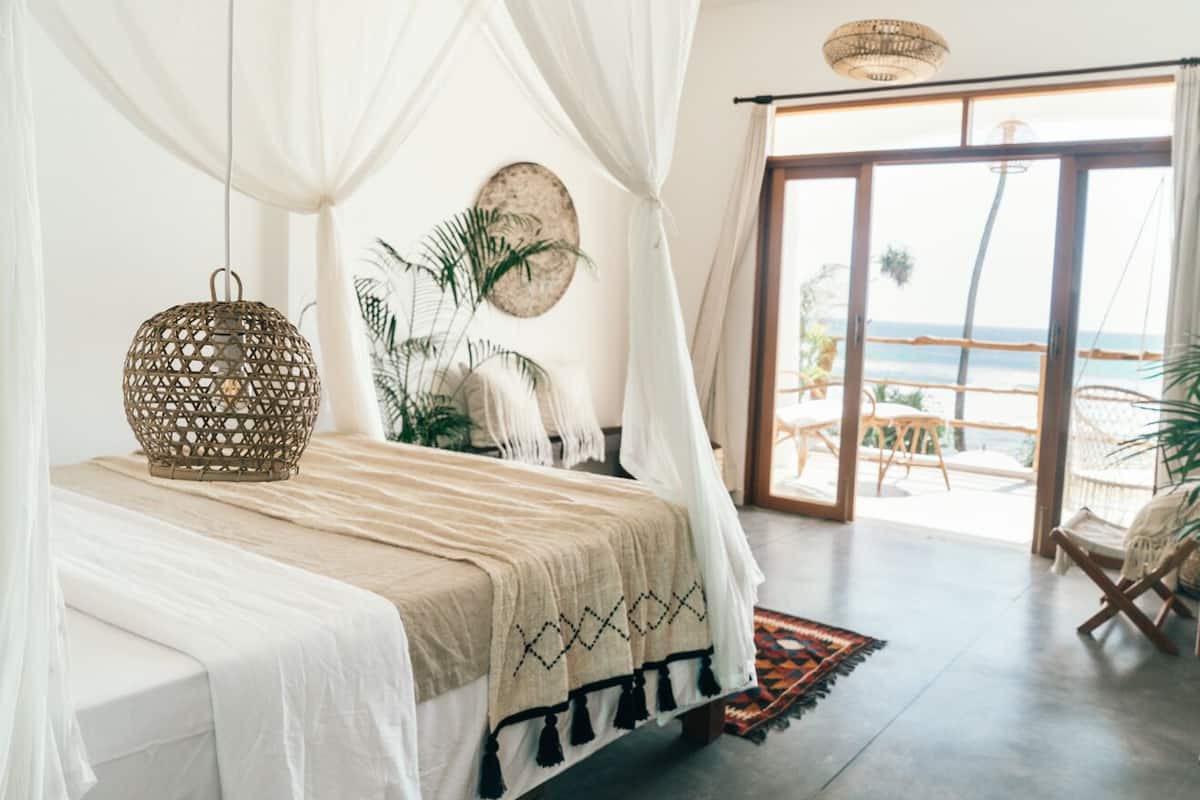 Een slaapkamer met een bed, een hanglamp, uitzicht op de oceaan en een balkon met een stoel.
