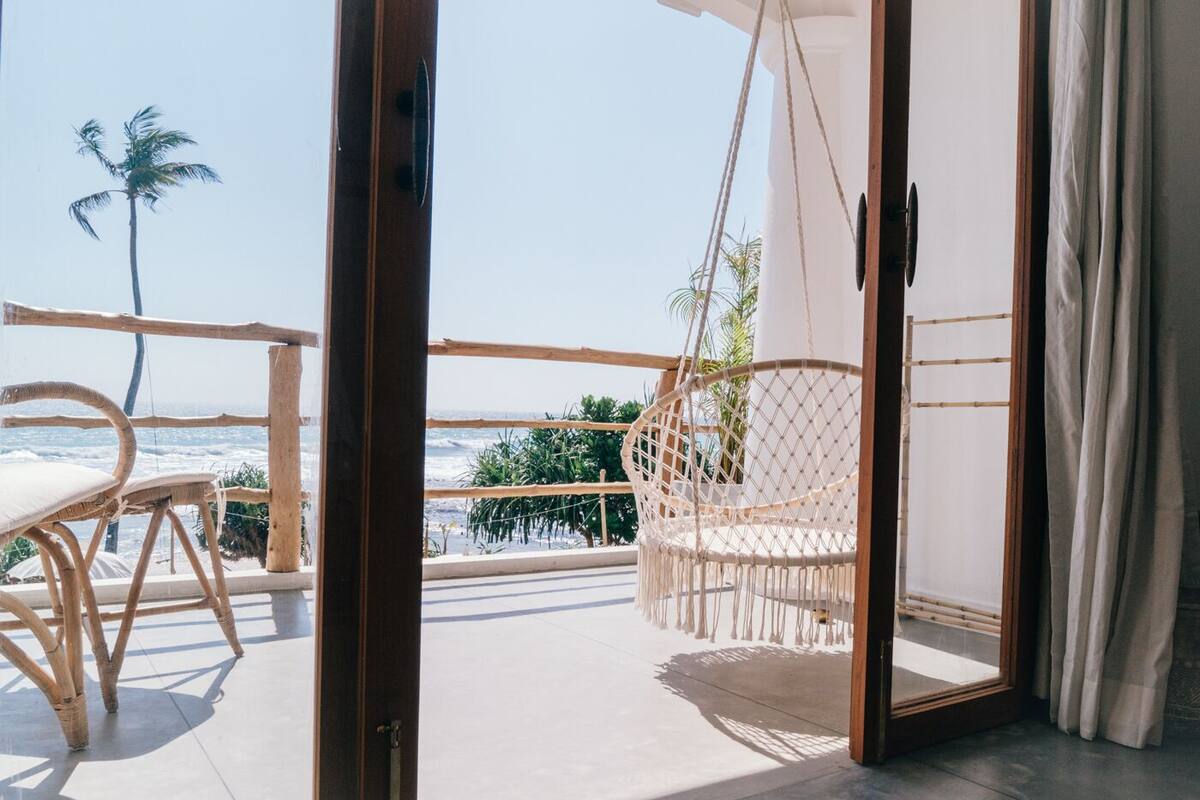 Een balkon met een rieten stoel, een hangstoel en uitzicht op de oceaan.
