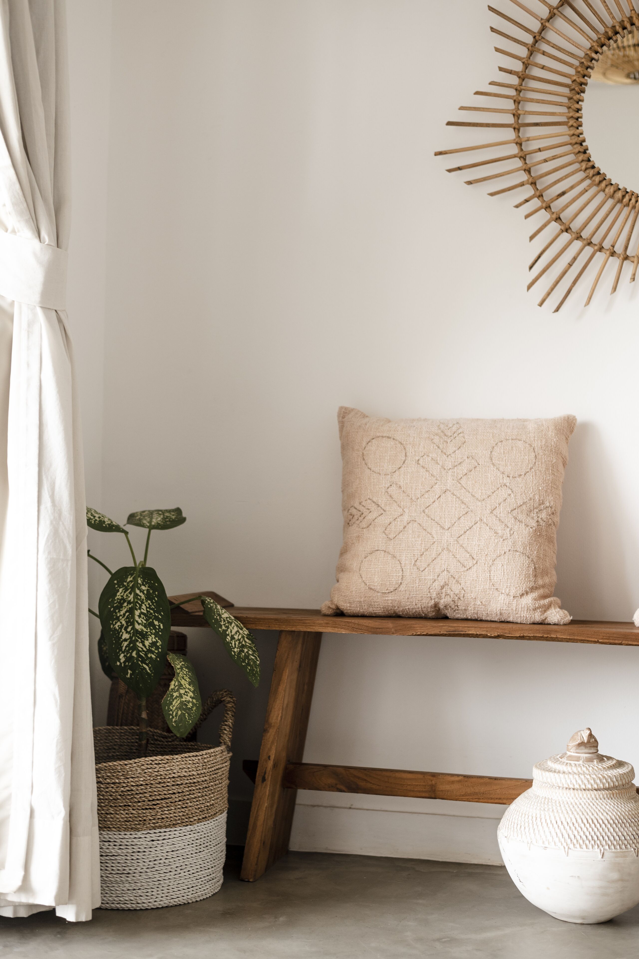A room with a wooden bench, a woven basket, a potted plant, and a decorative wall piece.