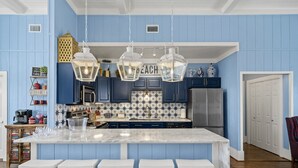 A kitchen with blue walls, white bar stools, and hanging lanterns. - New! Rare Mezzanine Deck, Hot Tub & Beach Views! (Crystal Beach)
