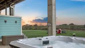 A hot tub with a glass of wine, a wooden bench, and a view of a grassy field and sunset. - New! Rare Mezzanine Deck, Hot Tub & Beach Views! (Crystal Beach)