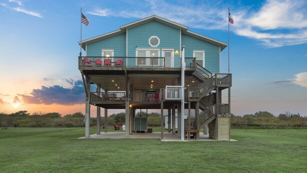 A two-story building with a balcony, a staircase, and a flag. - New! Rare Mezzanine Deck, Hot Tub & Beach Views! (Crystal Beach)