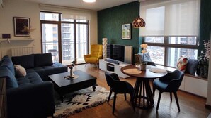 Un salon moderne comprenant un canapé, un fauteuil jaune, un téléviseur et un coin repas avec des chaises et une table.