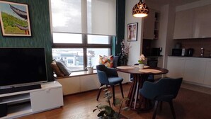 Un salon moderne avec un téléviseur, un coin salon, une table à manger et une cuisine en arrière-plan.
