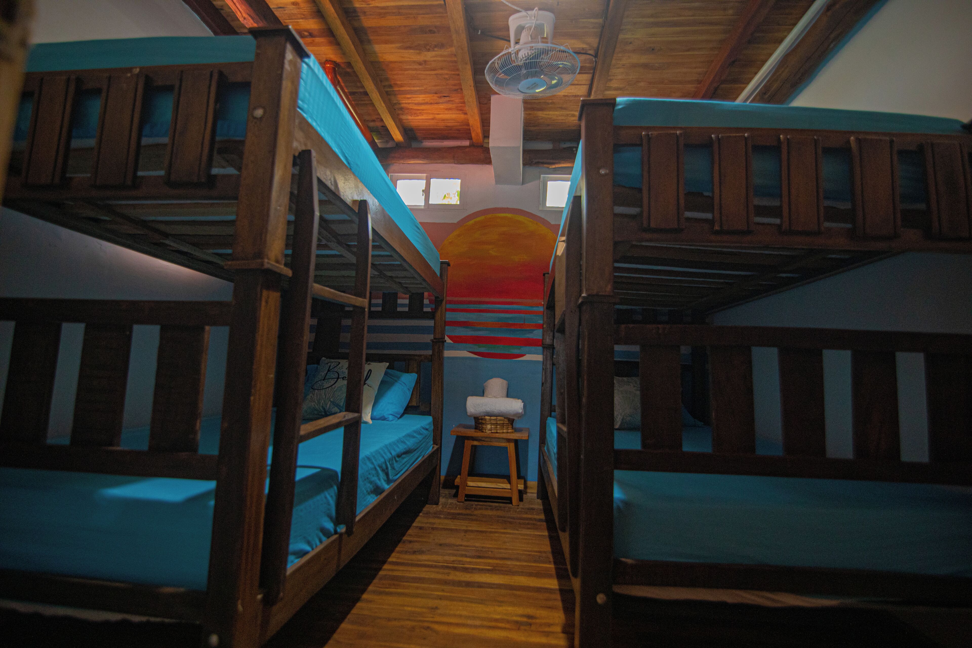 Quarto com beliches de madeira, roupa de cama azul e uma pequena mesa com uma cesta.