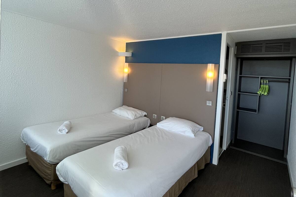A hotel room with two single beds, a wardrobe, and a small seating area.