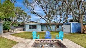 A backyard with a stone fire pit, three blue Adirondack chairs, a house, and a garage. - 4BR Home w/ Private Dock and Fenced Backyard and Firepit. Minutes from the Beach (St. Augustine)