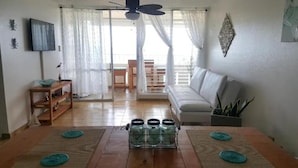 A living room with a sofa, a TV, a wooden table, and a glass cabinet with jars. - Luquillo beachfront apt., beautiful ocean view! (Luquillo)