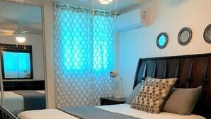 Un dormitorio con cama, mesita de noche, lámpara y televisión al fondo.