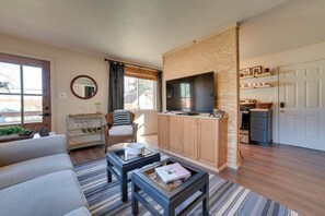 A modern living room with a sofa, coffee table, TV, and kitchen area. - Chic Harrison Home: Walk to Wilson State Park! (Harrison)