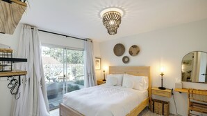 A bedroom with a large bed, a wooden headboard, bedside tables, a hanging light fixture, a window with curtains, and a view of the outdoors. - Monterey Bay 4BR, 3BA, Hot Tub Near Beaches & Golf (Seaside)