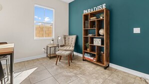 Ein Zimmer mit einer Türkis-farbenen Akzentwand, einem Holzregal mit der Aufschrift 'PARADISE', einem gepolsterten Sessel und einem kleinen Tisch mit einer Lampe.