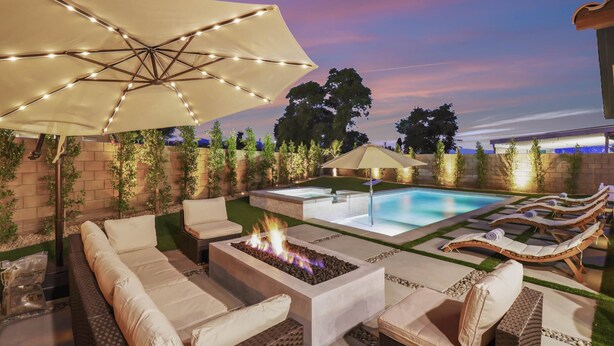 Eine Außenpatio mit Pool, Liegestühlen, Feuerstelle und Sonnenschirm.