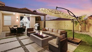 Eine Terrassenausstattung im Freien mit Feuerstelle, Sitzgelegenheiten und einem überdachten Bereich mit Grill.