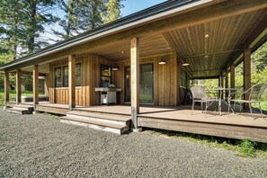 Ein überdachter Außenbereich mit Holzboden, einem Tisch, Stühlen und einer Küchenzeile mit Spüle und Schränken.