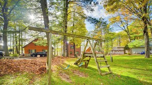Une aire de jeux avec des balançoires et un toboggan, entourée d’arbres et d’une structure en bois.