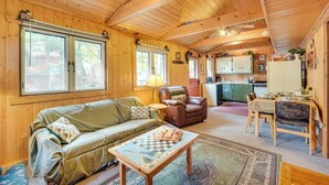 L’intérieur chaleureux d’un chalet avec un plafond en bois, un canapé vert, un fauteuil en cuir marron, une table à manger et un coin cuisine.