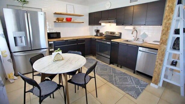 A modern kitchen with a marble table, black chairs, stainless steel appliances, and a wooden shelf. - Beach Getaway - Upstairs
 (St. Augustine)