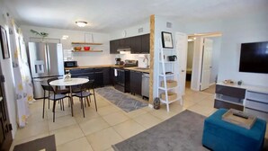A modern kitchen with dark cabinets, a white countertop, and a dining area with a round table and chairs. - Beach Getaway - Upstairs
 (St. Augustine)