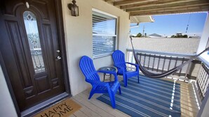 A wooden deck with a blue-striped mat, two blue Adirondack chairs, a small round table, a hammock, and a 'Happy Home' mat at the entrance. - Beach Getaway - Upstairs
 (St. Augustine)