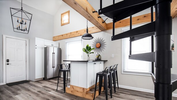 Una cocina moderna con armarios blancos, una isla de madera, taburetes negros y una lámpara colgante.