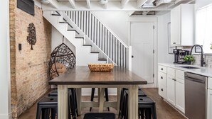 Una cocina moderna con una mesa de madera, taburetes negros y una escalera que sube a otro nivel.