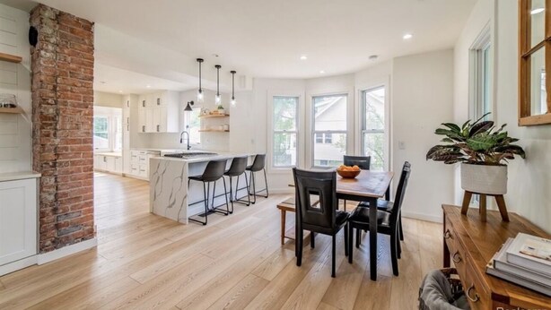 A modern kitchen with white cabinets, a brick accent wall, and a dining area with a wooden table and chairs. - Charming Plymouth retreat • hot tub • fire pit

 (Plymouth)