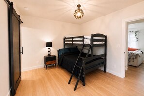 Un dormitorio con una cama individual superpuesta, una mesita de noche con lámpara y una puerta que da a otra habitación.