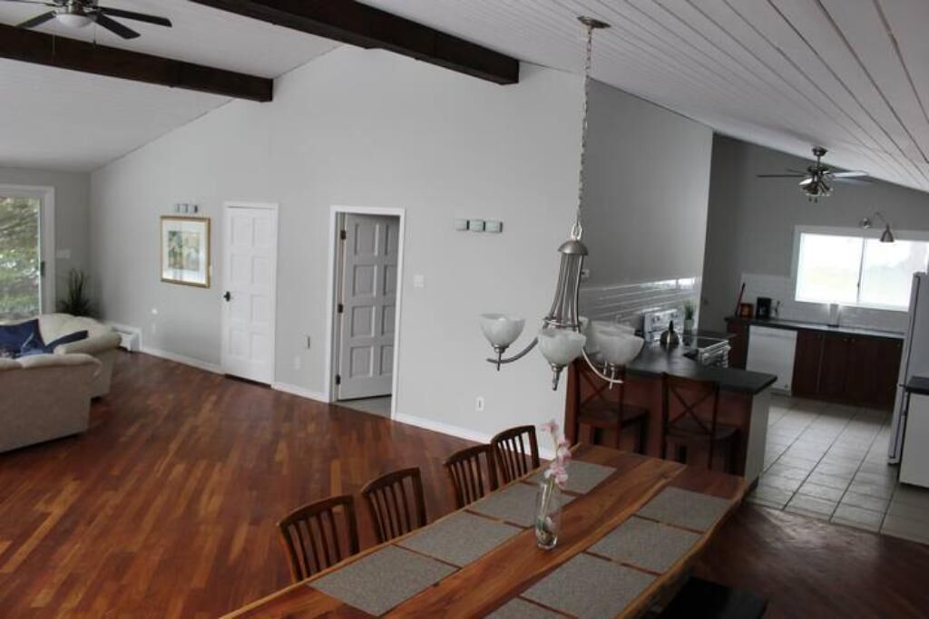 A spacious living area with a wooden dining table, a sofa, and a kitchen in the background.