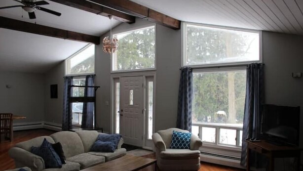 A living room with a sofa set, a coffee table, and a television. There are large windows and a ceiling fan. - Country Oasis in the Village (Elora)