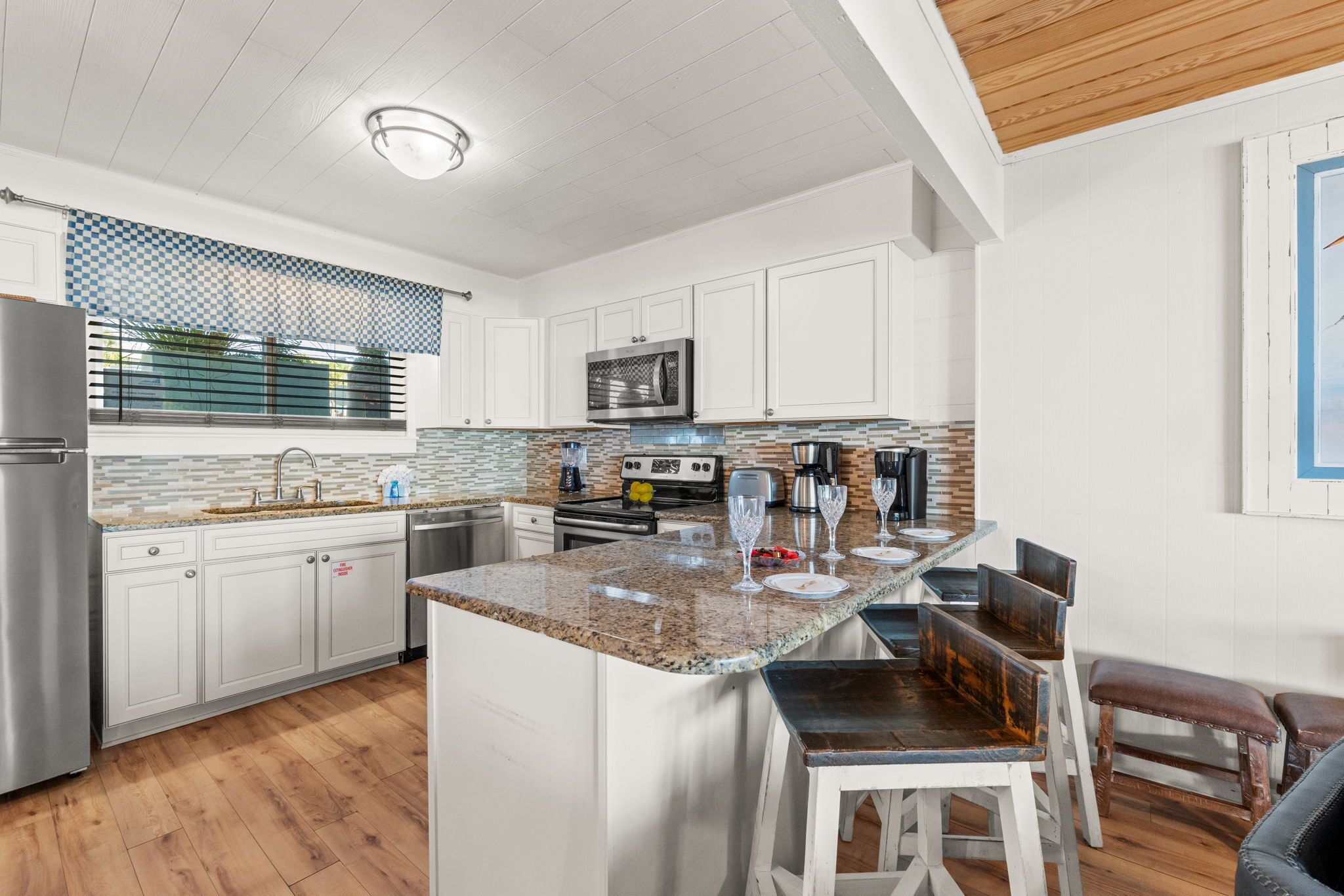 A modern kitchen with white cabinets, a granite countertop, and a wooden ceiling.