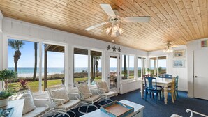 A room with a wooden ceiling, large windows, a dining area, and a view of the beach. - Sunny Beach by Book That Condo (Panama City Beach)