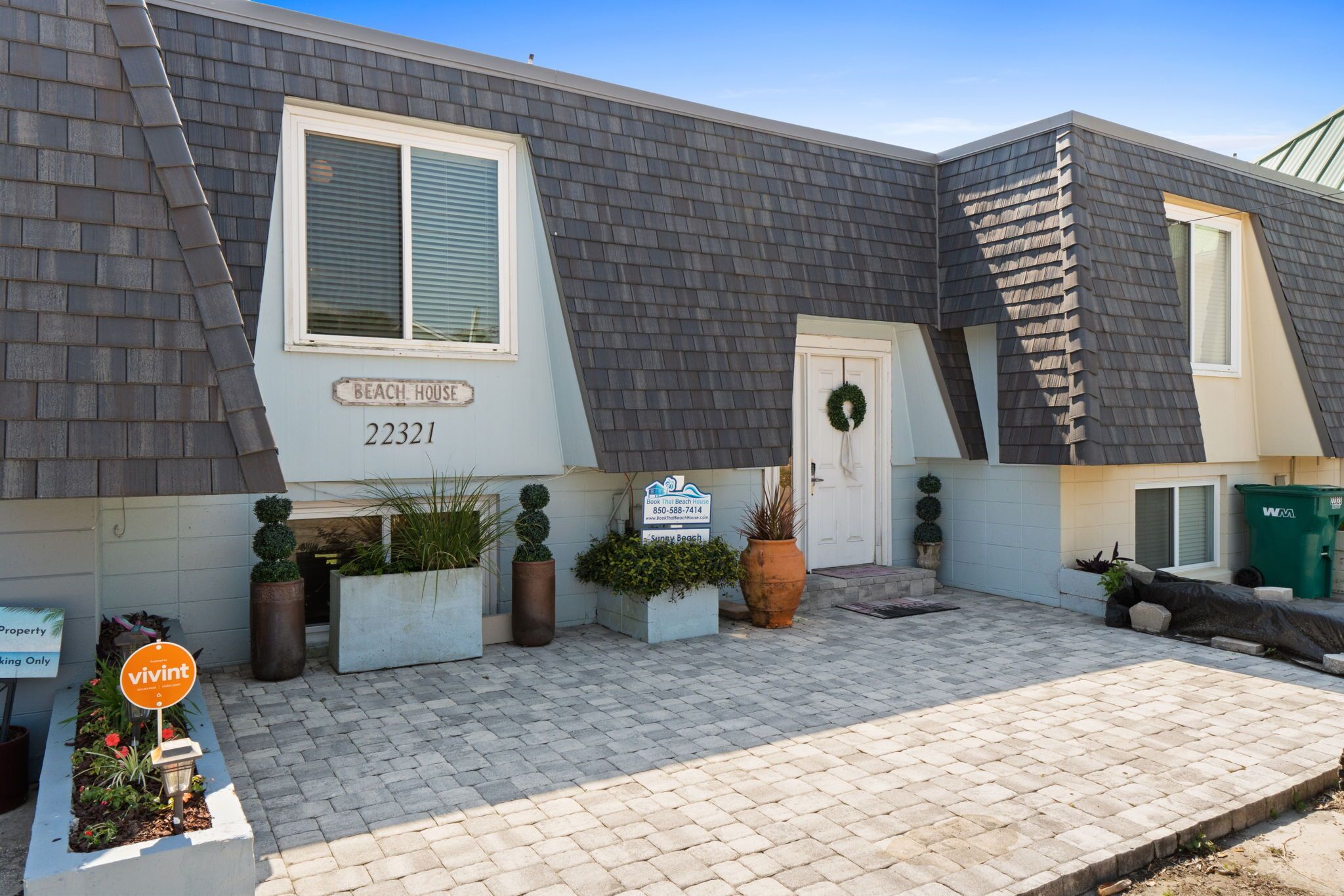 Una propiedad residencial con techo de tejas grises, una puerta principal adornada con un adorno navideño, y un letrero que dice 'Beach House 22321'.