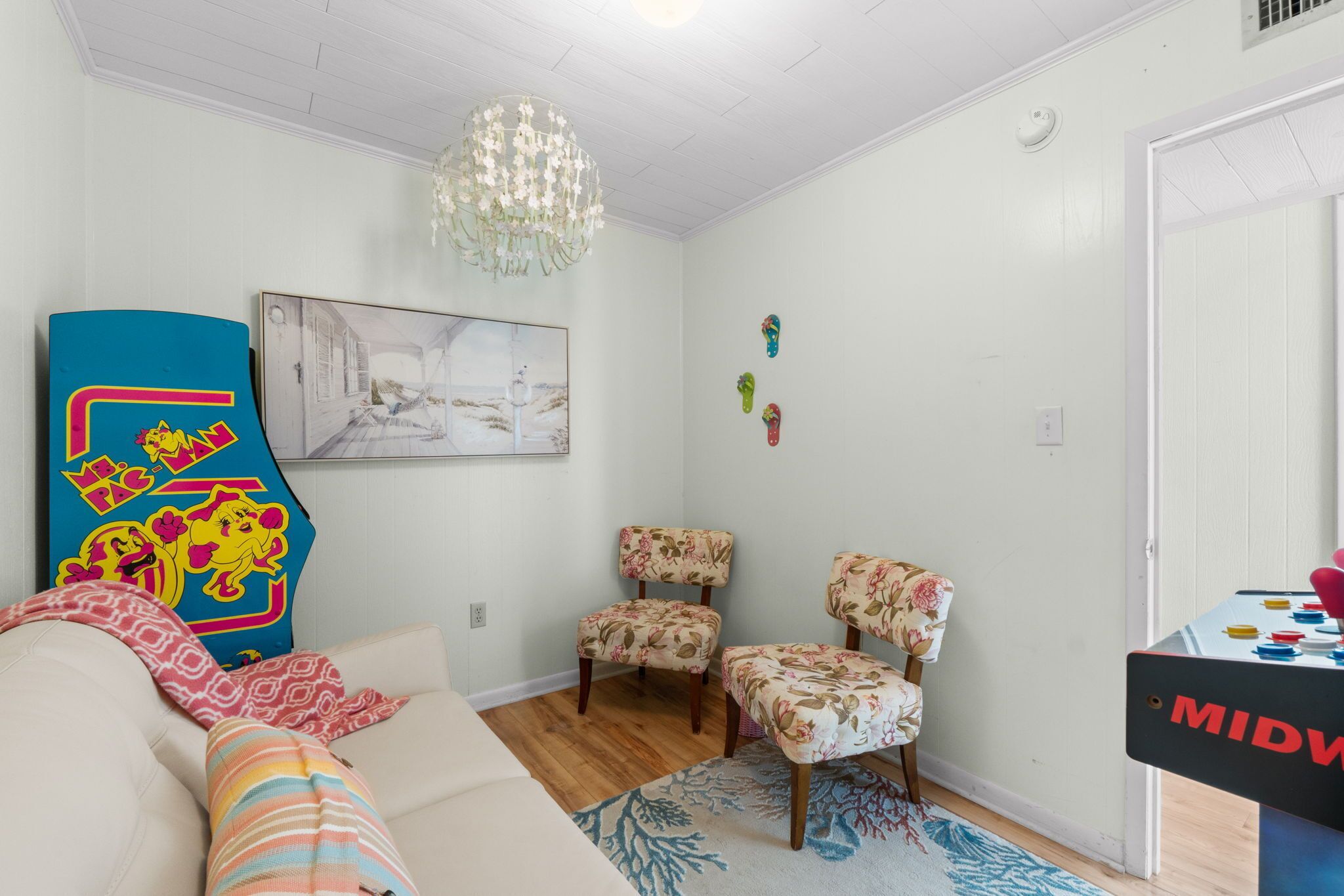 A room with a white ceiling, a chandelier, a sofa, two floral chairs, a table with a game, and a painting on the wall.