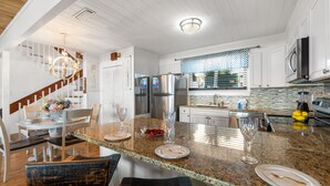 A modern kitchen with granite countertops, stainless steel appliances, and a dining area with a wooden staircase. - Sunny Beach by Book That Condo (Panama City Beach)